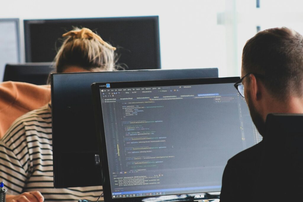 zwei Personen sitzen sich am Schreibtisch vor ihren PCs gegenüber